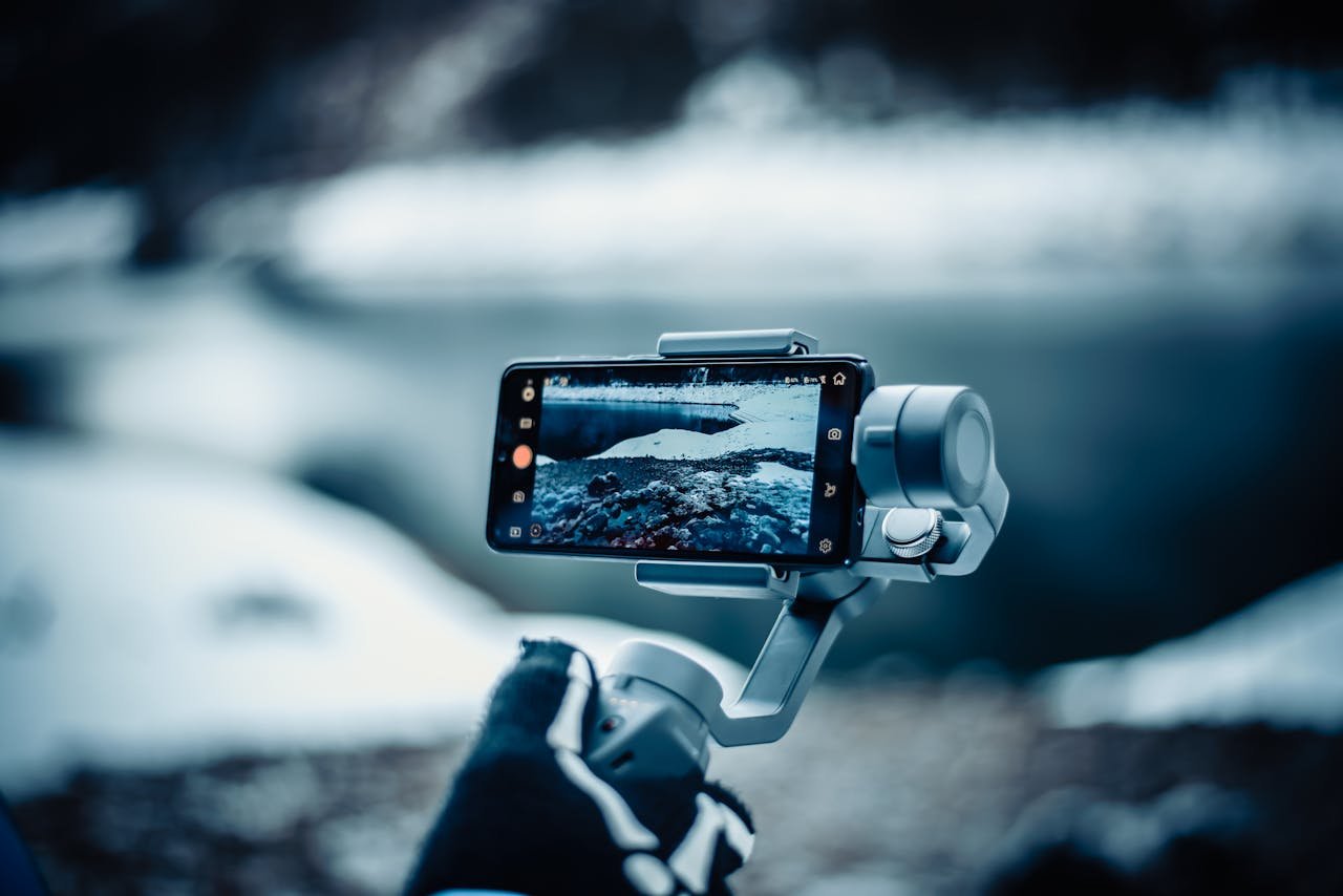 our-services-01 A smartphone mounted on a stabilizer capturing a snowy winter scene outdoors.
