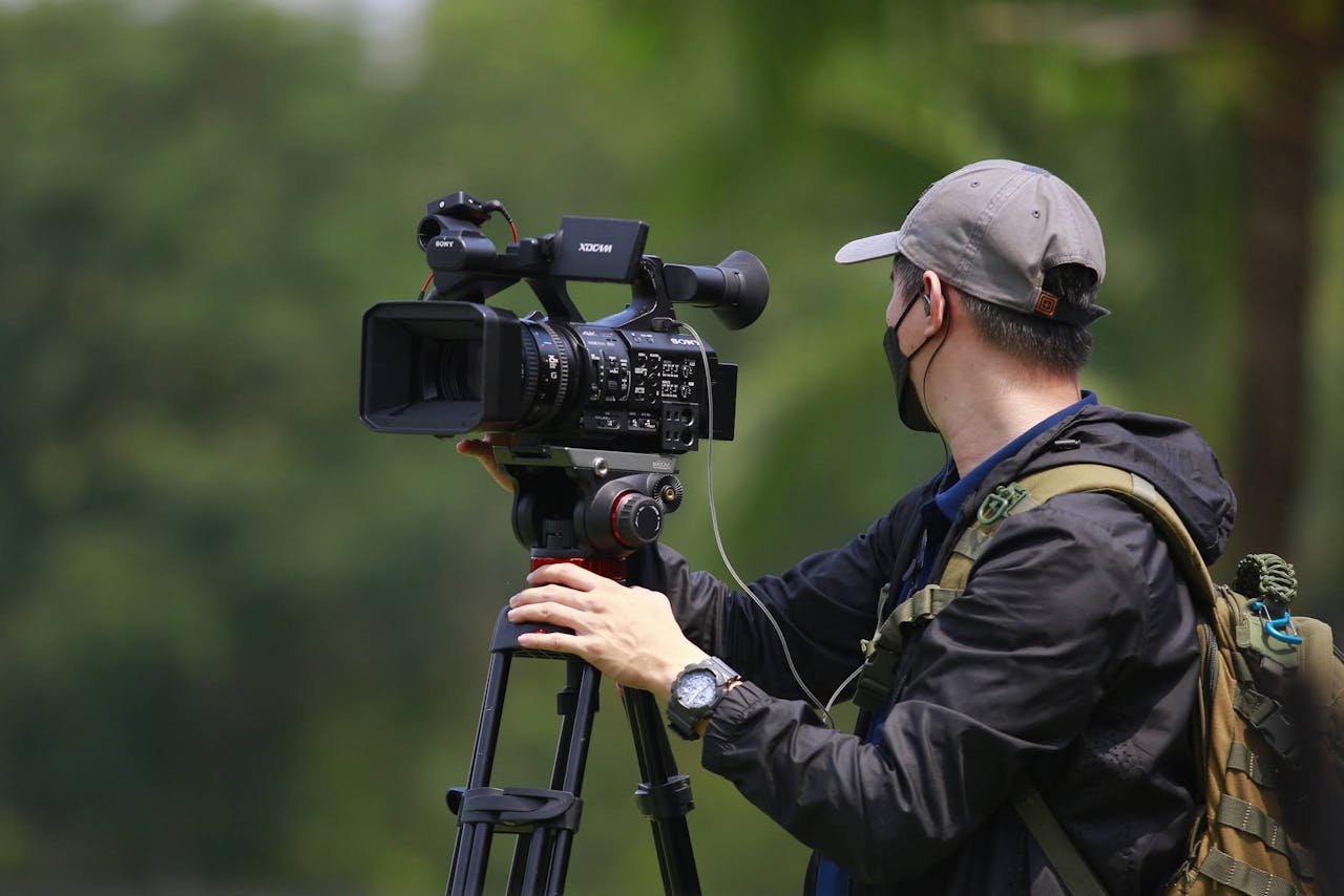 our-services-04 Cinematographer in action outdoors, adjusting a professional video camera on a tripod.